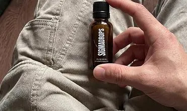 Frasco ámbar original de SigmaDrops con tapa negra, sostenido entre los dedos