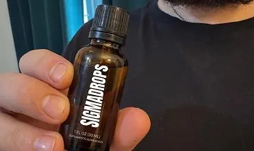 Frasco original de SigmaDrops de 30 ml en la mano, con la leyenda «Suplemento alimenticio» y «1 fl oz (30 ml)»